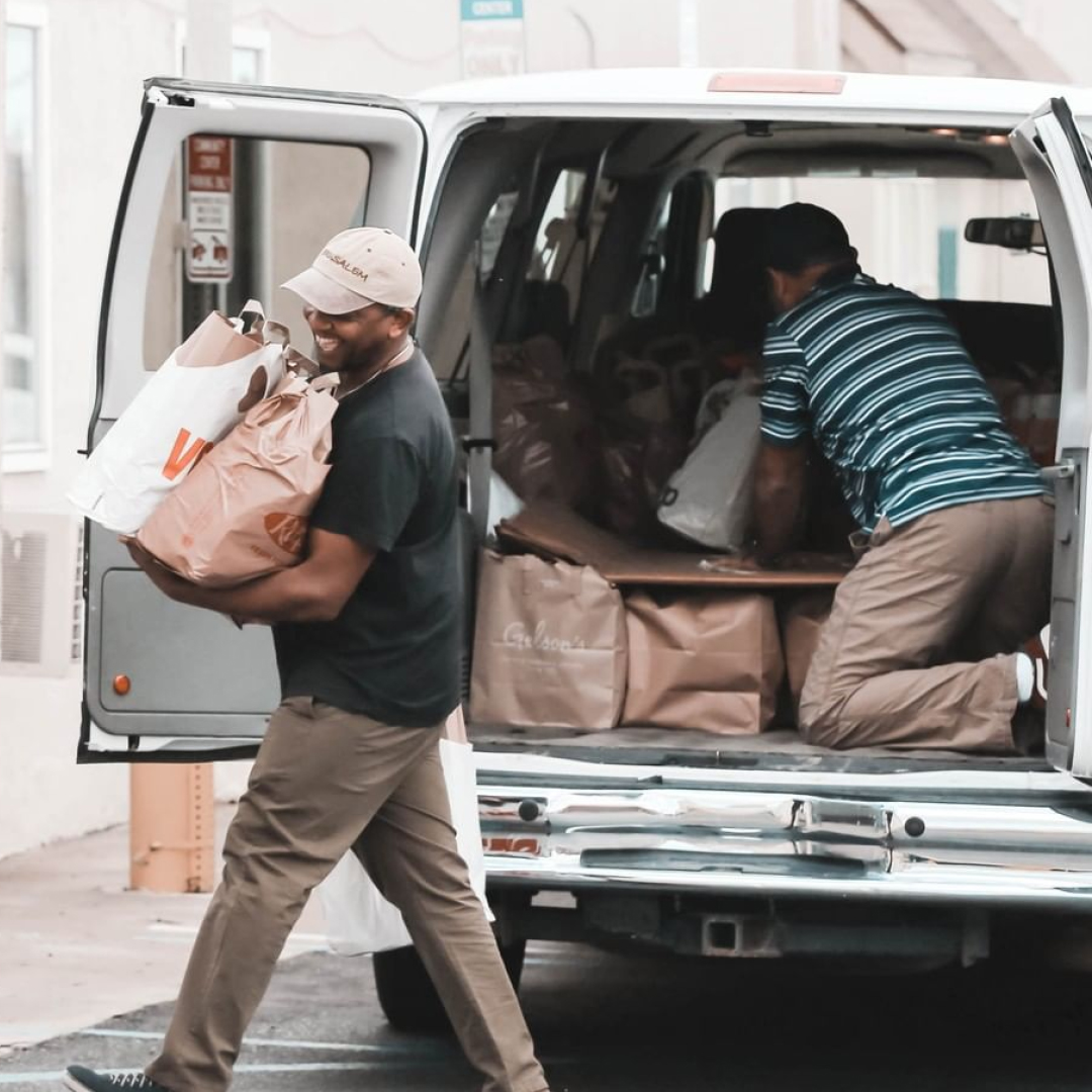 Two adults unloading packaged food from a van