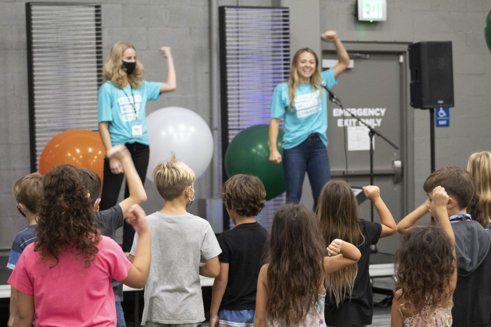 Two people on stage leading a crowd of children