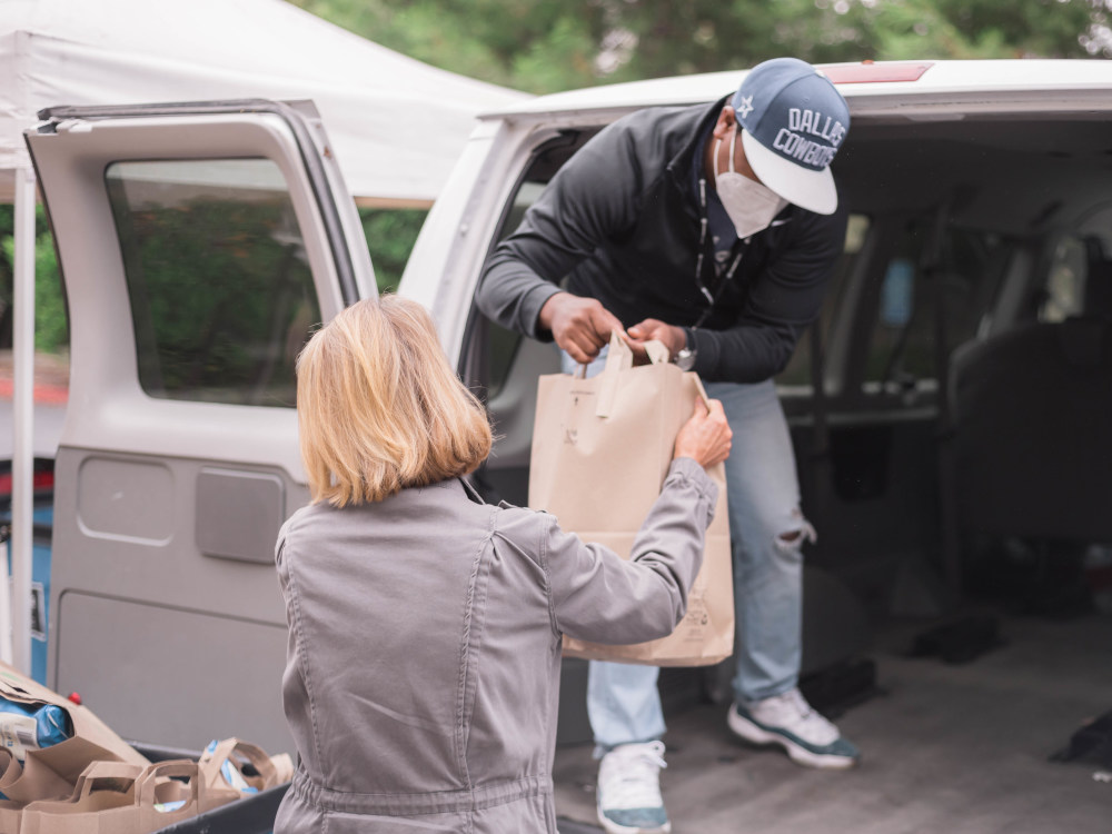 Person handing a bag of groceries from a van to another person